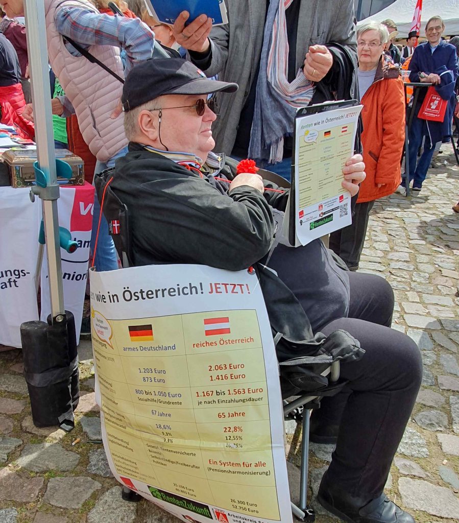 Eine Person sitzend mit RentenZukunft Plakat am Stuhl und einer Unterschriftenliste in der Hand.
