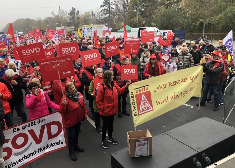 Von der Bühne herunter fotografiert auf die Demonstrierenden. Vorne ein Transparent "SOVD-Heidekreis" und eins "Wer Rentner quält wird nicht gewählt" Im Vordergrund steht ein Karton mit der Forderung.